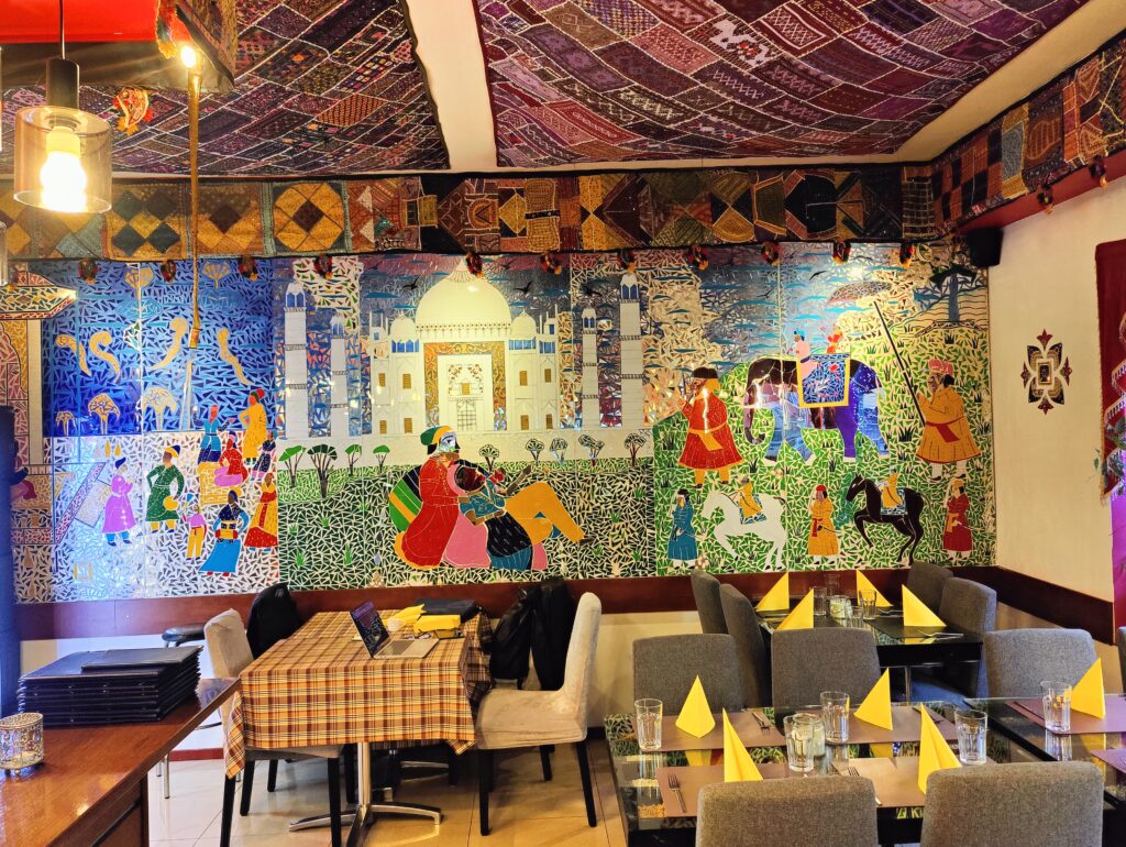 Innenraum von India4U Bern mit traditioneller indischer Wanddekoration und gemütlichen Sitzplätzen